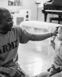 A service member in an Army shirt playing with his young child at home