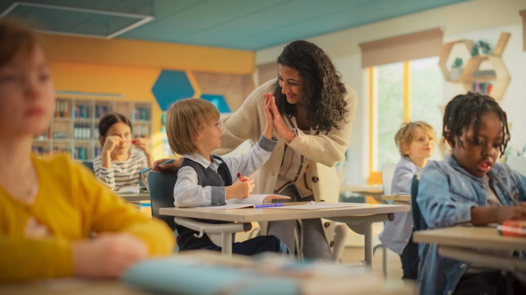 Elementary teacher giving a student a high five in a bright classroom
